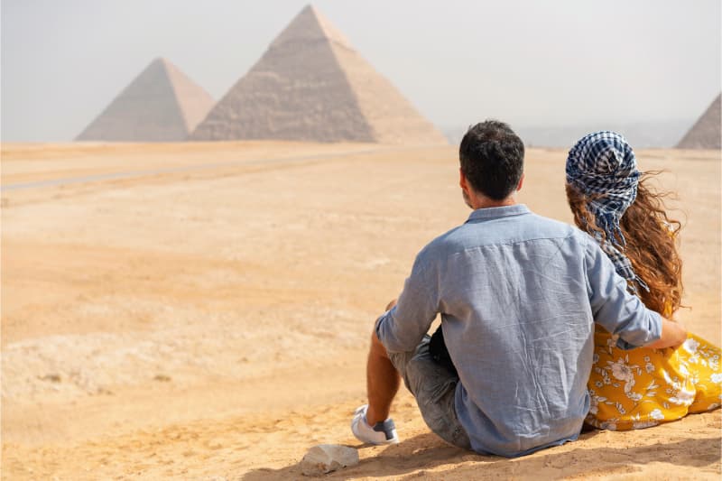 Unvergesslicher Moment vor Ägyptens Wahrzeichen Paar sitzt in der Wüste mit Blick auf die Pyramiden von Gizeh