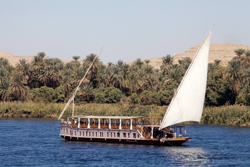 Romantische Nilfahrt mit Dahabiya durch Ägypten Traditionelles Segelboot fährt auf dem Nil entlang grüner Uferlandschaft
