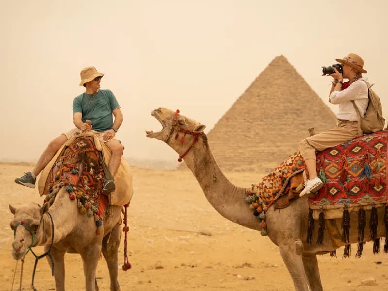 Pirámides de Guiza Turistas de vacaciones montando camellos frente a las pirámides. Egipto, El Cairo - Guiza.