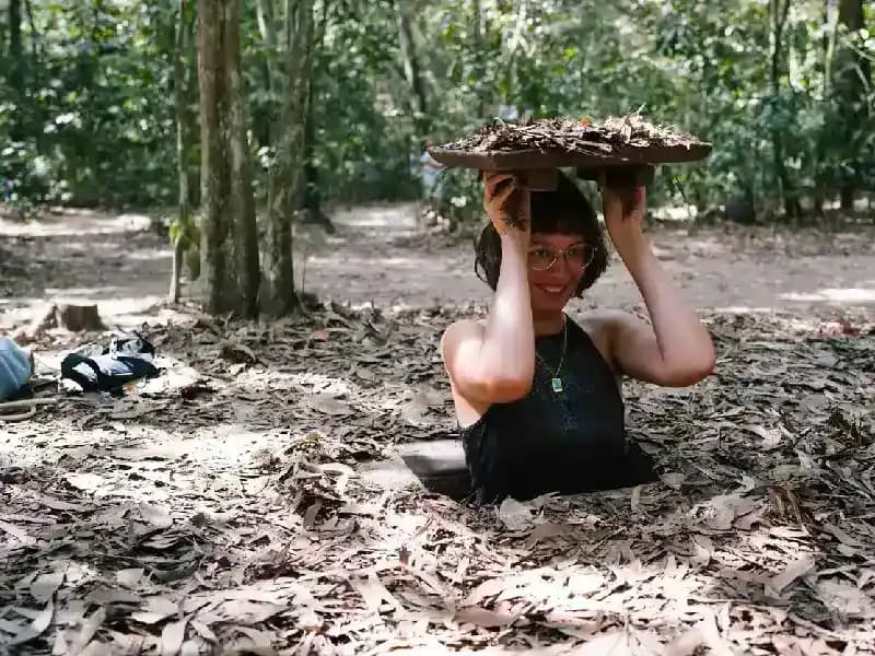 Túneis de Cu Chi, Vietnã mulher-sorridente-saindo-de-entrada-camuflada-dos-tuneis-de-cu-chi-segurando-a-tampa-de-folhas-na-floresta-do-vietna