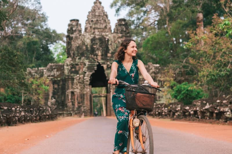 Portão Sul de Angkor Thom, Camboja mulher-sorridente-andando-de-bicicleta-em-frente-ao-portao-de-pedra-esculpido-de-angkor-thom-no-camboja