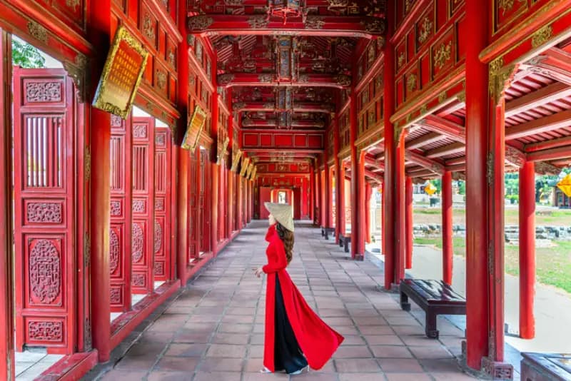 Corredor da Cidadela Imperial de Hue mulher-com-ao-dai-vermelho-e-chapeu-conico-em-corredor-imperial-ornamentado-da-cidadela-de-hue-vietna