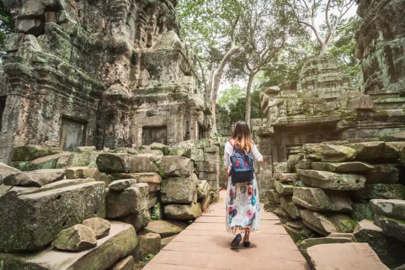 Templo de Ta Prohm, Angkor, Camboja mulher-caminhando-por-passarela-de-madeira-entre-ruinas-de-pedra-cobertas-de-musgo-no-templo-de-ta-prohm-camboja