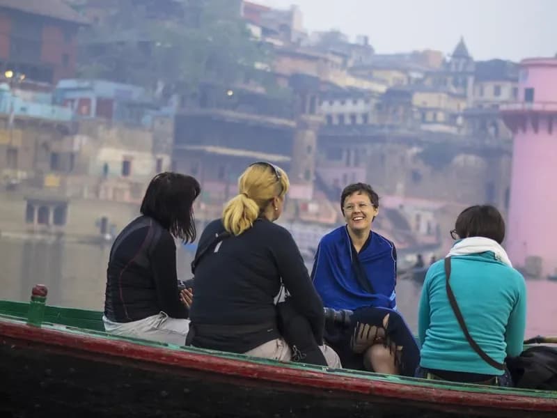 Rio Ganges, Varanasi turistas-sorridentes-em-barco-navegando-pelo-rio-ganges-com-os-ghats-de-varanasi-ao-fundo-na-india