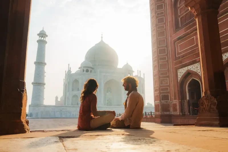 Taj Mahal casal-sentado-de-pernas-cruzadas-em-frente-ao-taj-mahal-ao-amanhecer-emoldurado-por-um-arco-de-arenito-vermelho-agra-india