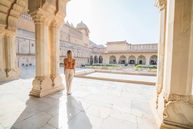 Forte Amber em Jaipur mulher-caminhando-por-um-patio-ensolarado-com-colunas-esculpidas-no-forte-amber-jaipur-india