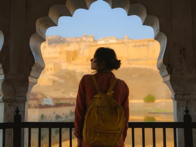 Jaipur, Índia mulher-com-mochila-amarela-observando-a-vista-de-um-forte-historico-atraves-de-um-arco-esculpido-em-jaipur-india