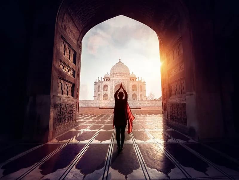 Taj Mahal ao pôr do sol silhueta-de-mulher-com-bracos-erguidos-admirando-o-taj-mahal-ao-por-do-sol-emoldurada-por-um-arco-escuro-agra-india