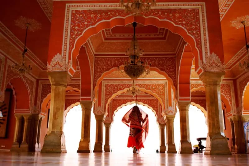 Palácio da Cidade de Jaipur mulher-com-sari-vermelho-caminhando-por-um-salao-ornamentado-com-arcos-vermelhos-e-brancos-no-palacio-da-cidade-de-jaipur-india