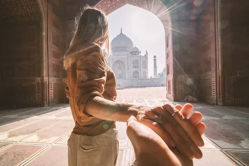 Taj Mahal em Agra mulher-segurando-a-mao-de-outra-pessoa-em-direcao-ao-taj-mahal-iluminado-pelo-sol-atraves-de-um-arco-agra-india
