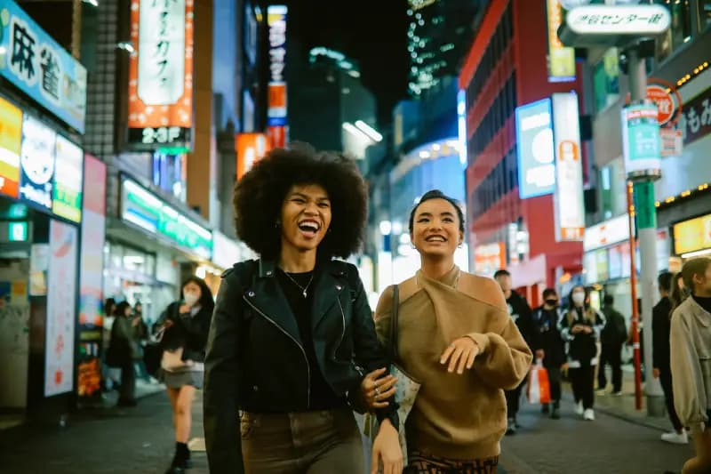 Tóquio duas-mulheres-sorrindo-caminhando-juntas-por-uma-rua-movimentada-a-noite-em-toquio-japao-cercadas-por-letreiros-neon-coloridos-e-luzes-da-cidade
