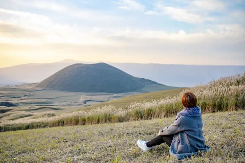 Monte Aso em Kumamoto mulher-sentada-em-um-campo-observando-uma-colina-vulcanica-ao-entardecer-na-regiao-do-monte-aso-kumamoto-japao