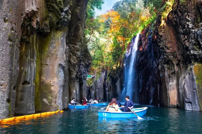 Desfiladeiro de Takachiho pessoas-remando-em-barcos-azuis-pelo-desfiladeiro-de-takachiho-com-uma-cachoeira-e-paredes-rochosas-cobertas-de-vegetacao-em-miyazaki-japao