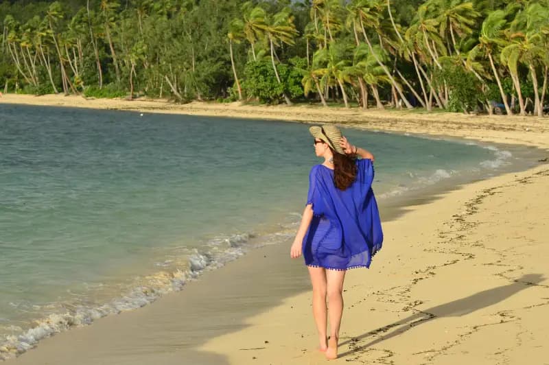 Tropical beach on a Fiji island woman-in-a-blue-dress-walking-barefoot-along-a-tropical-beach-with-palm-trees-and-turquoise-water-on-an-island-in-fiji
