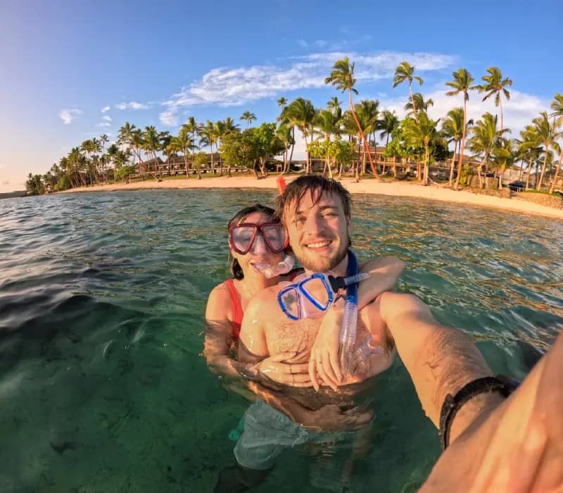 Snorkeling in Fiji couple-taking-a-selfie-while-snorkeling-in-clear-turquoise-water-with-a-tropical-beach-in-fiji-in-the-background