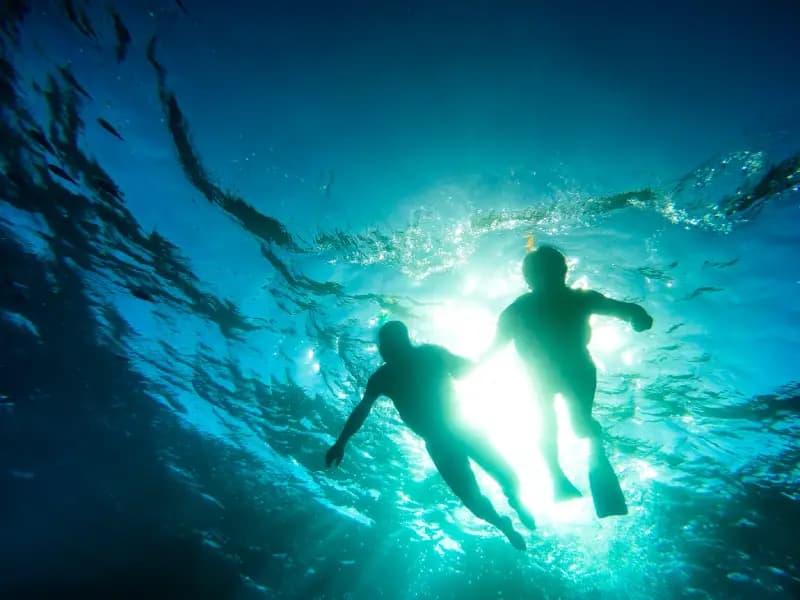 underwayer in fiji underwater-silhouette-of-two-people-swimming-with-fins-against-glowing-sunlight-in-turquoise-wate