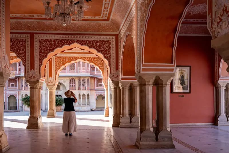 City Palace of Jaipur woman-walking-through-a-red-and-white-ornately-decorated-arched-hall-at-the-city-palace-of-jaipur-india