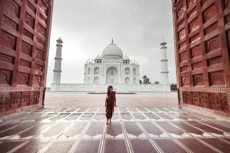Taj Mahal, Agra woman-in-a-red-dress-walking-through-a-grand-red-sandstone-gateway-with-the-taj-mahal-in-the-background-agra-india