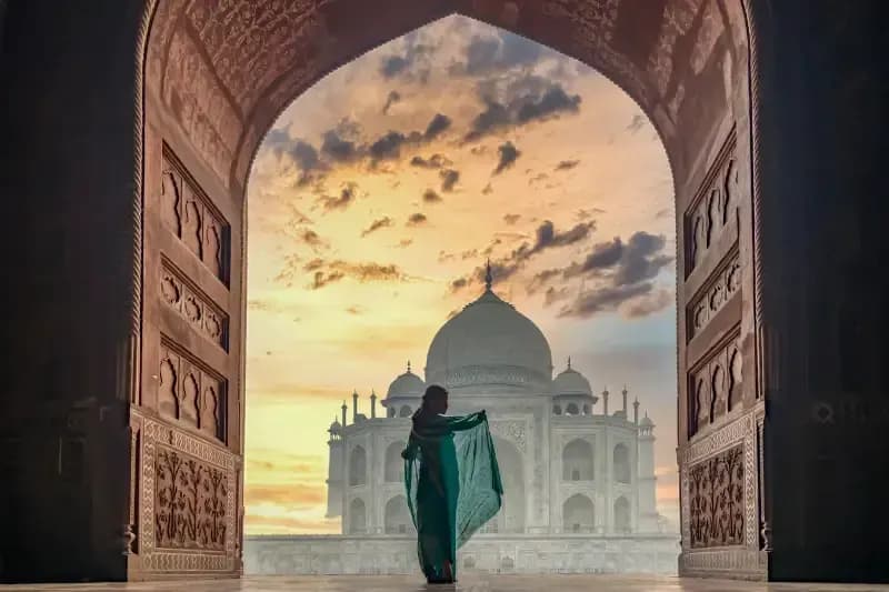 Taj Mahal silhouette-of-a-woman-in-a-flowing-green-sari-admiring-the-taj-mahal-under-a-dramatic-sunset-sky-framed-by-a-carved-archway-agra-india