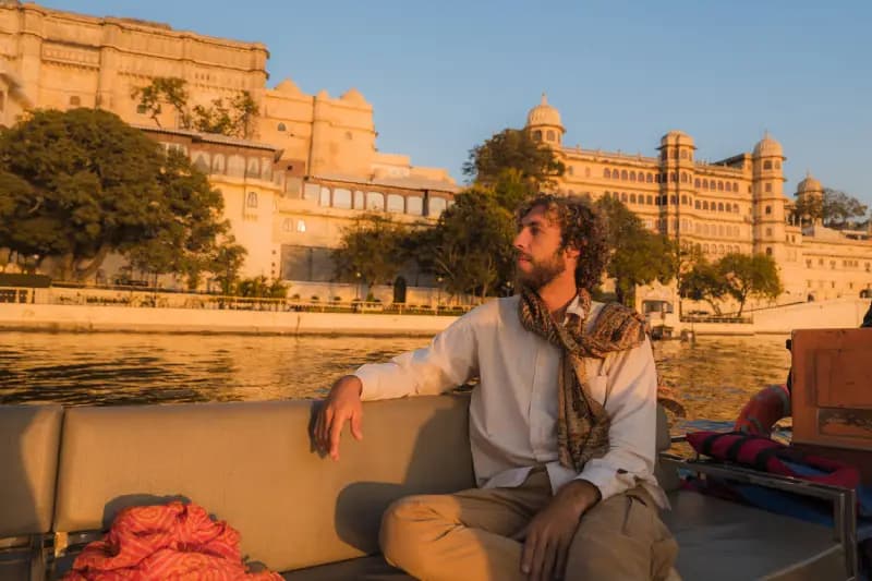 City Palace of Udaipur man-sitting-on-a-boat-overlooking-the-city-palace-of-udaipur-reflected-on-the-lake-at-golden-hour-india