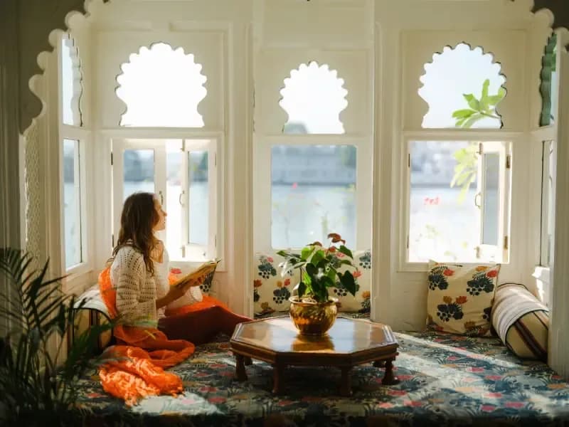 "Lake Haveli in Udaipur woman-reading-by-arched-windows-overlooking-the-lake-at-a-traditional-haveli-in-udaipur-india